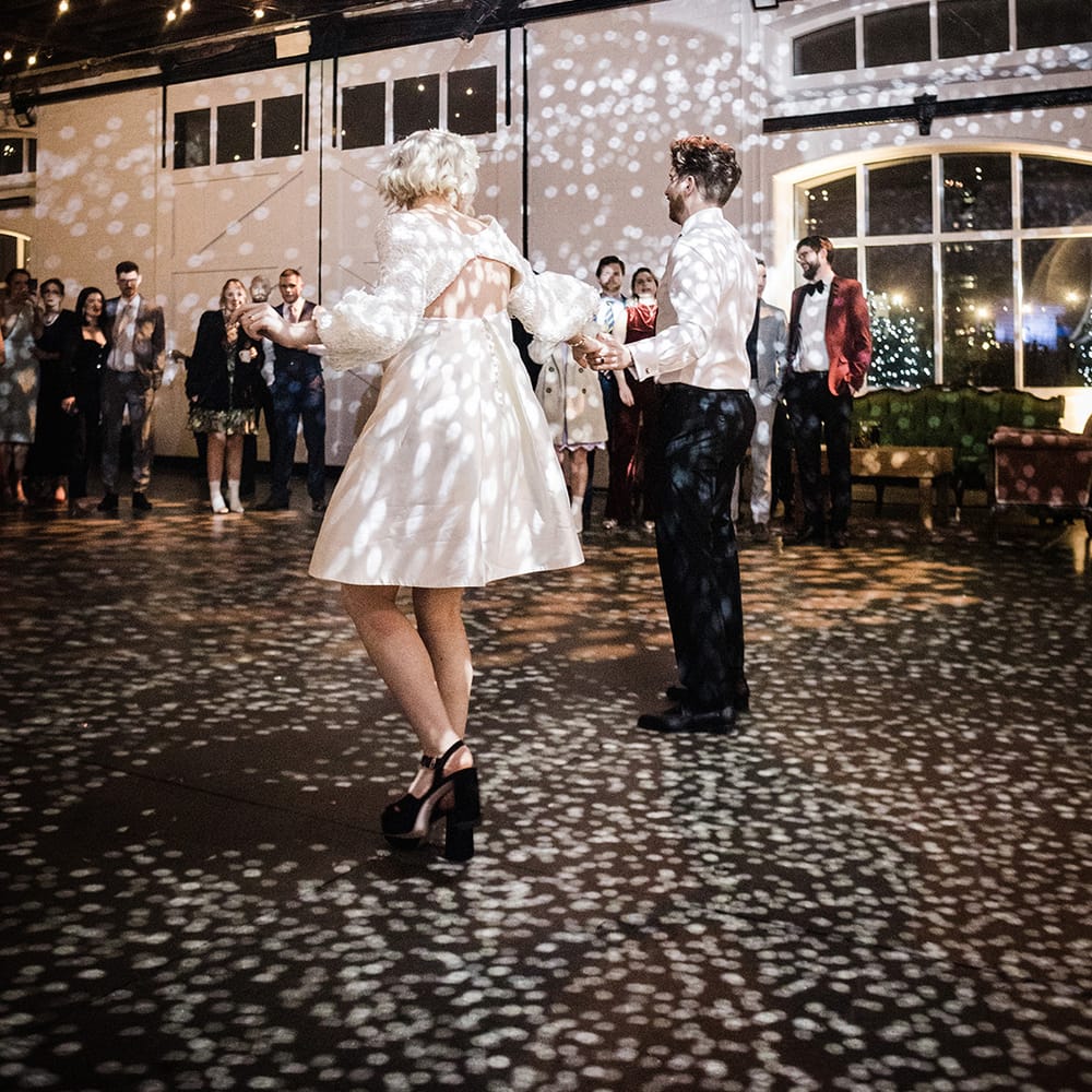 Bride in short wedding dress with groom in shirt and suit trousers have their first dance 