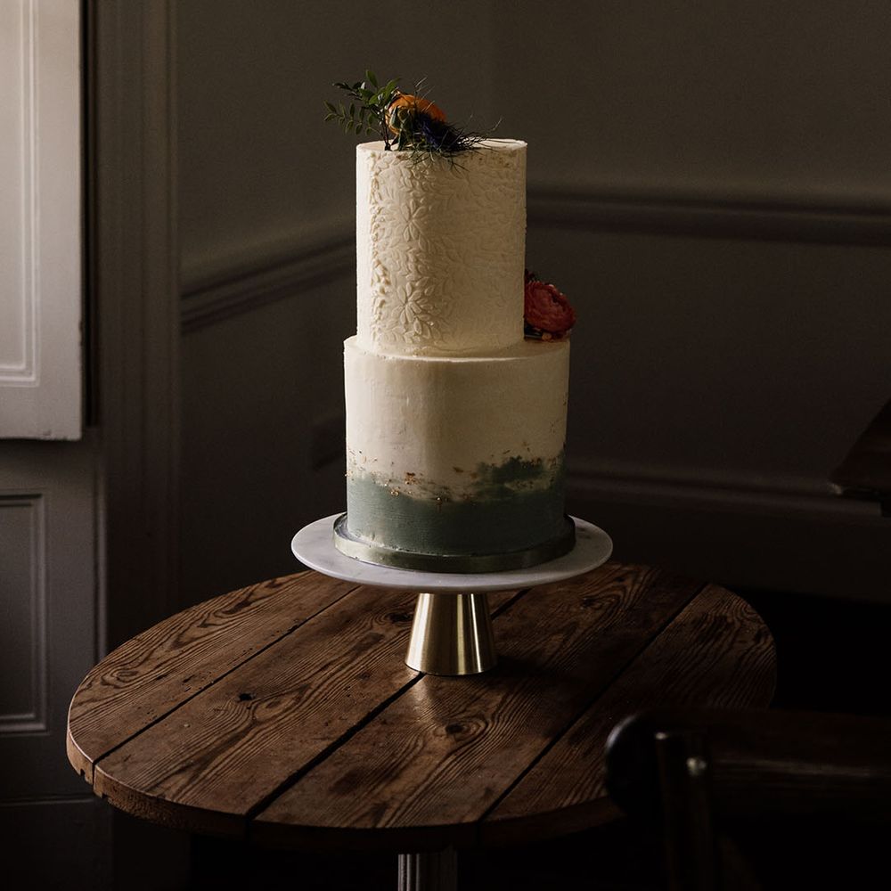 Two tier tall wedding cake with green ombre icing and gold flakes and flower icing with real flower decoration 