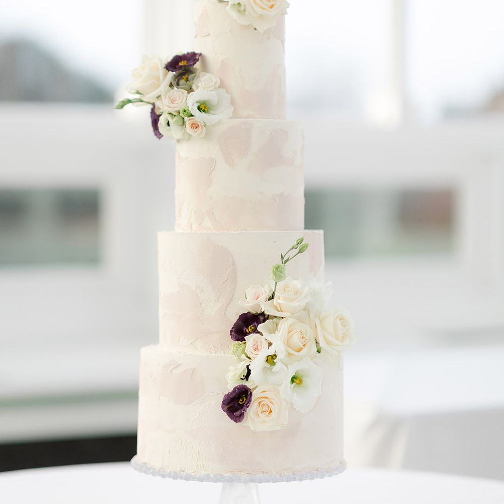 Four tier wedding cake finished with pale pink and white frosting complete with floral decoration 