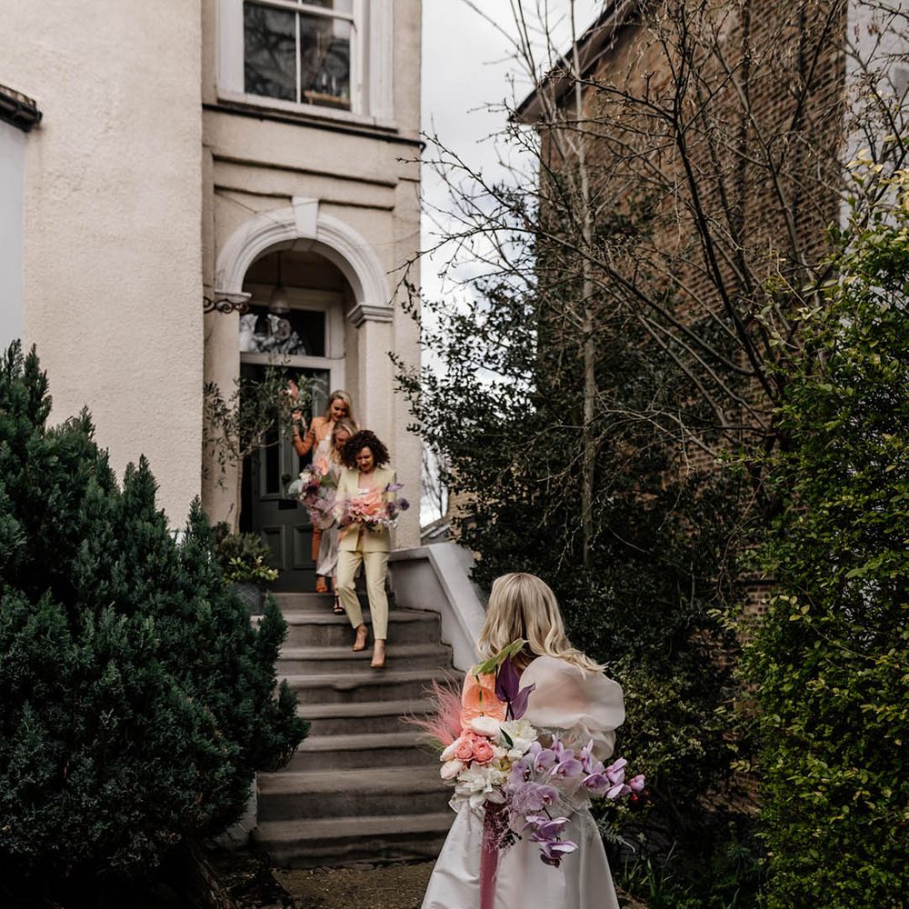 bridal party in colourful bridesmaid suits walking down steps to meet the bride in a Jesus Peiro wedding dress