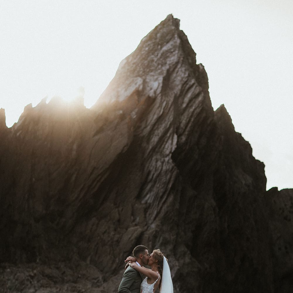 Sun shines across rocks as bride & groom kiss outdoors during couples portraits on the rocks 