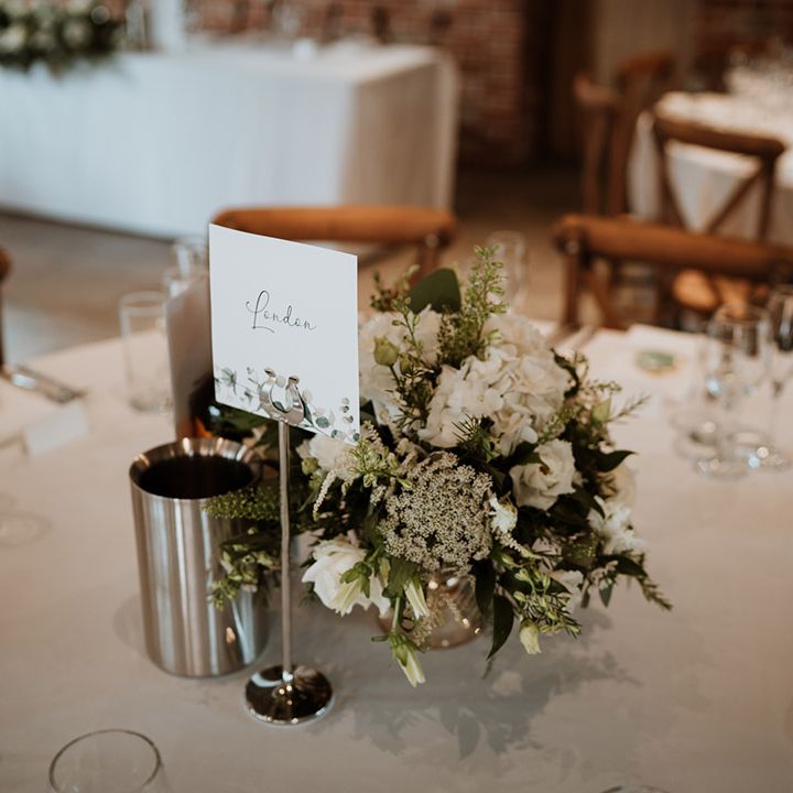 White card table name with foliage design with simple white flower centrepiece 