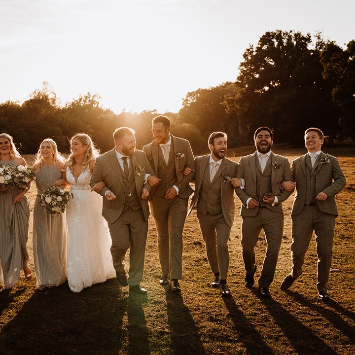 The bridal party and the groomsmen walk with the bride and groom during golden hour laughing together 