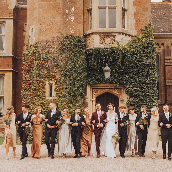 Bride & groom walk with wedding party who wear mismatched bridesmaid dresses in Autumnal colours 