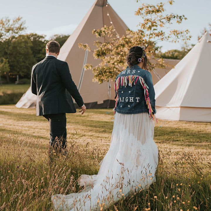 Bride in colourful personalised denim jacket walks with her groom