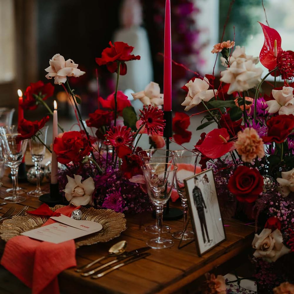 Personalised drawing of the couple in gold frame on magenta, disco themed wedding tablescape with red, off white and pink roses, red tapered candles, gold plates and disco ball decorations 