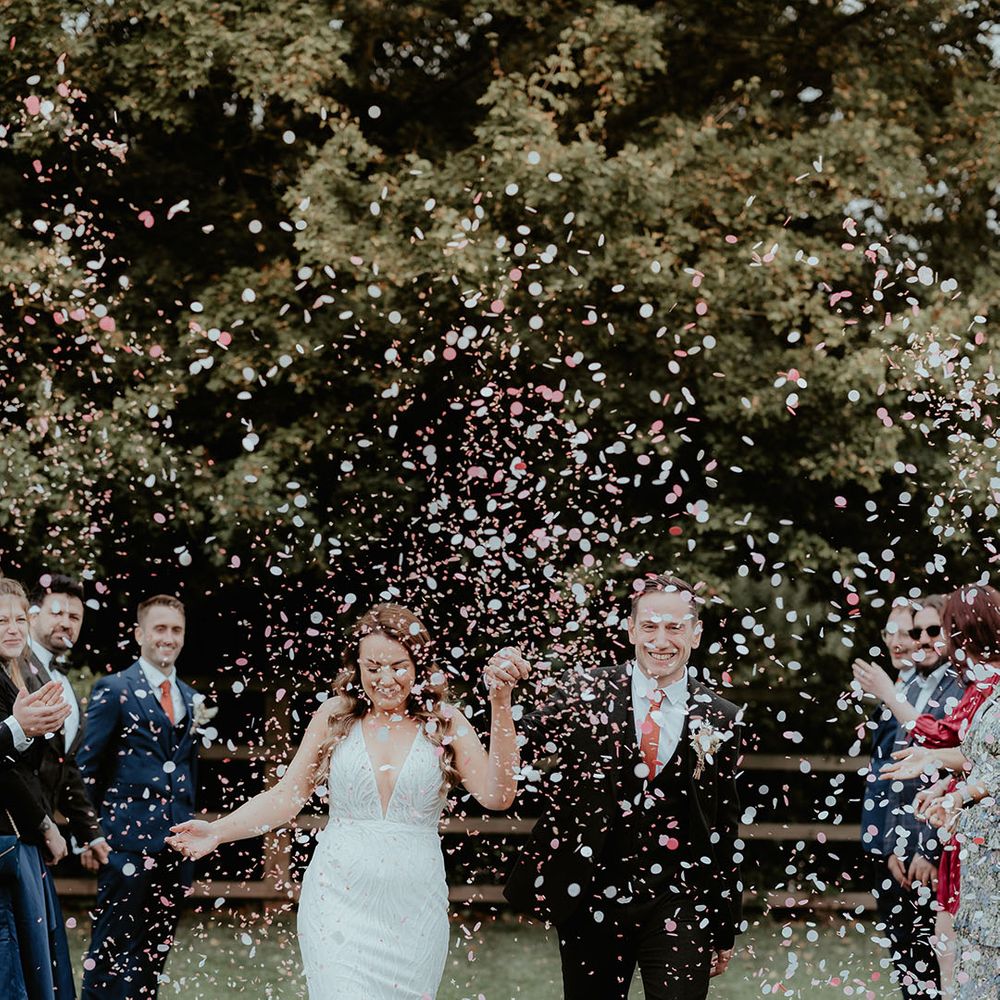 The bride and groom walk hand in hand for their confetti moment after their wedding 