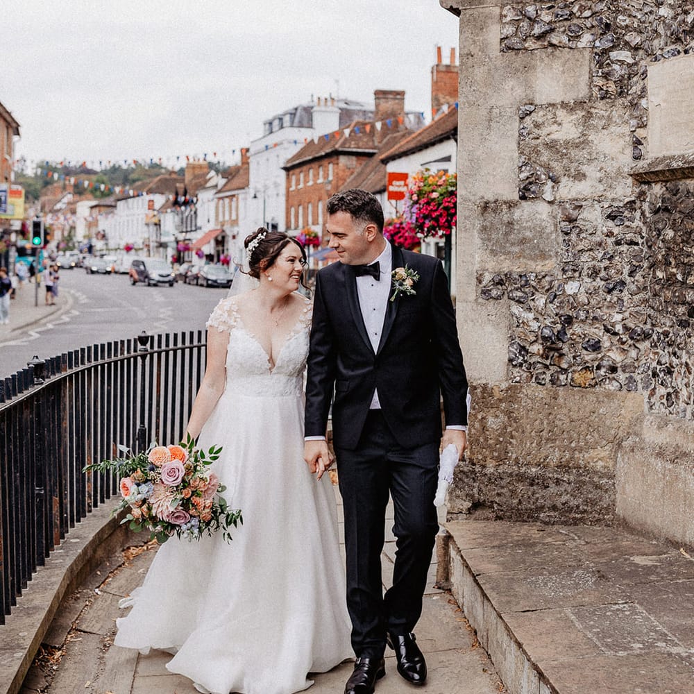 The bride in a flower Suzanne Neville wedding dress with the groom in black tuxedo holding spring wedding bouquet 