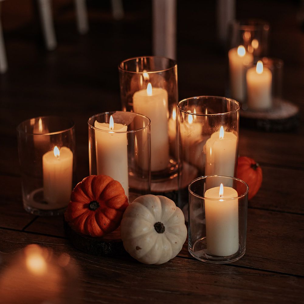 Cream pillar candles rest in glass hurricane vases with cute mini pumpkin decor for boho autumnal wedding at Milling Barn