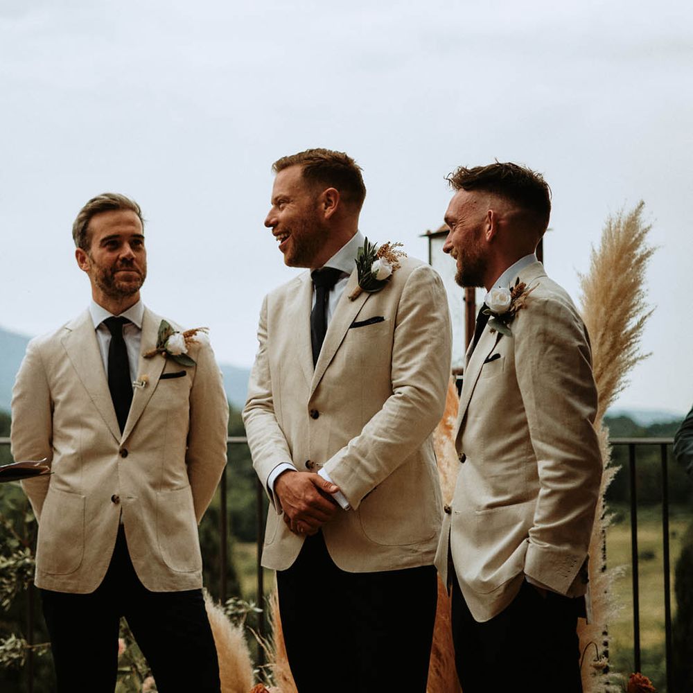 Groom and groomsmen in linen suits with white rose boutonnières at destination wedding in Tuscany