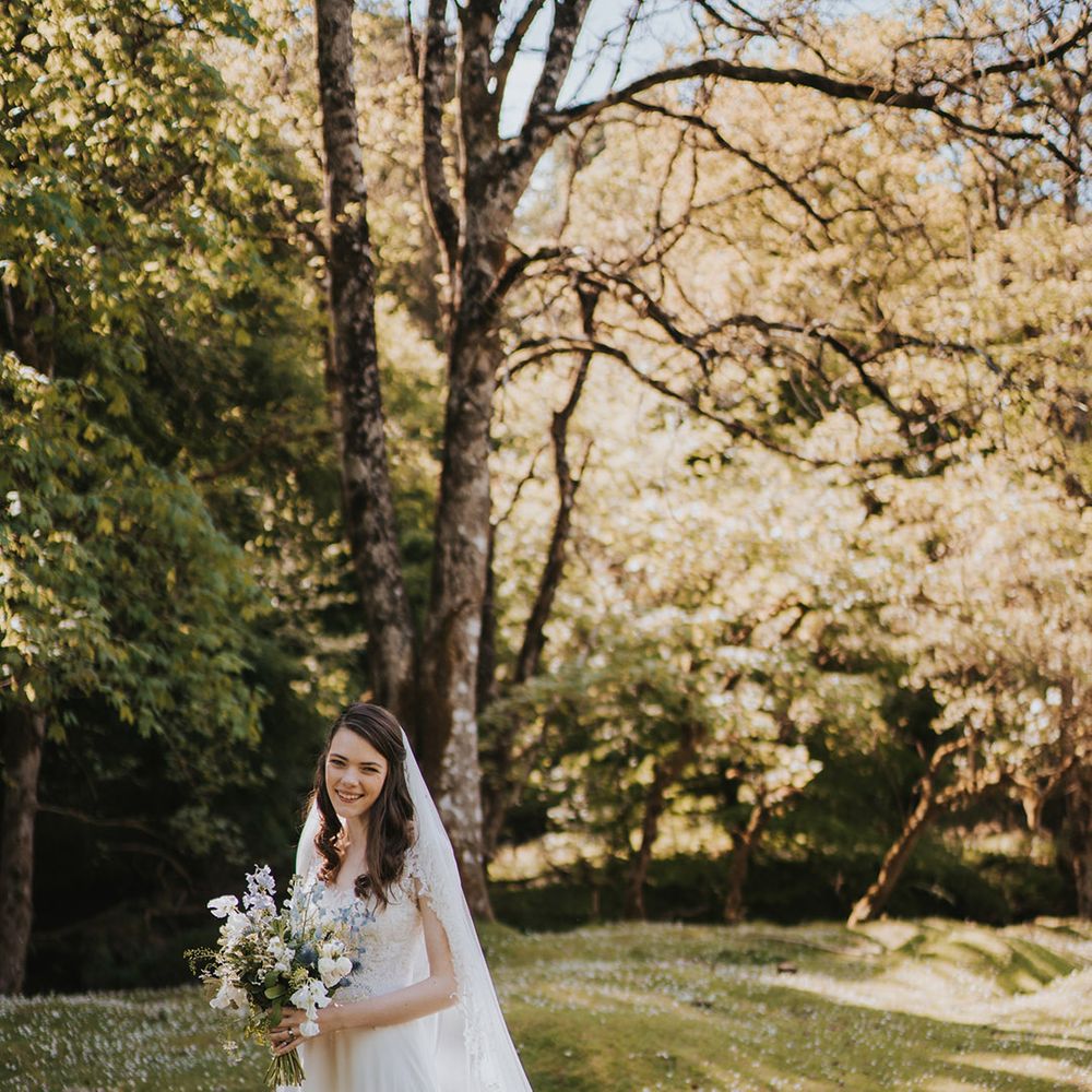 Bride in beaded wedding dress with embroidered cathedral length wedding veil holding white and blue bouquet 