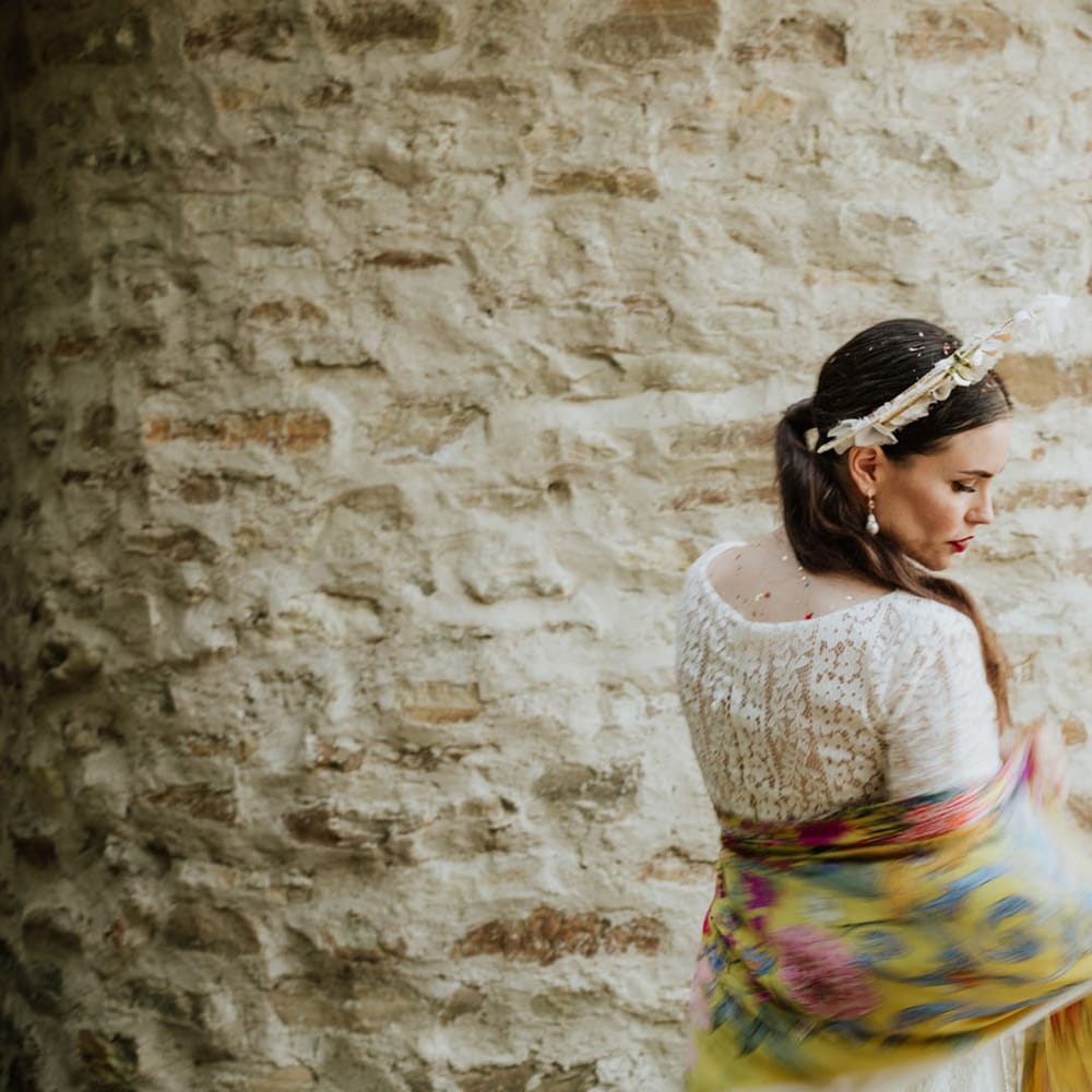 Bride at rustic wedding venue wearing white lace wedding dress, boho bridal crown and yellow floral pashmina