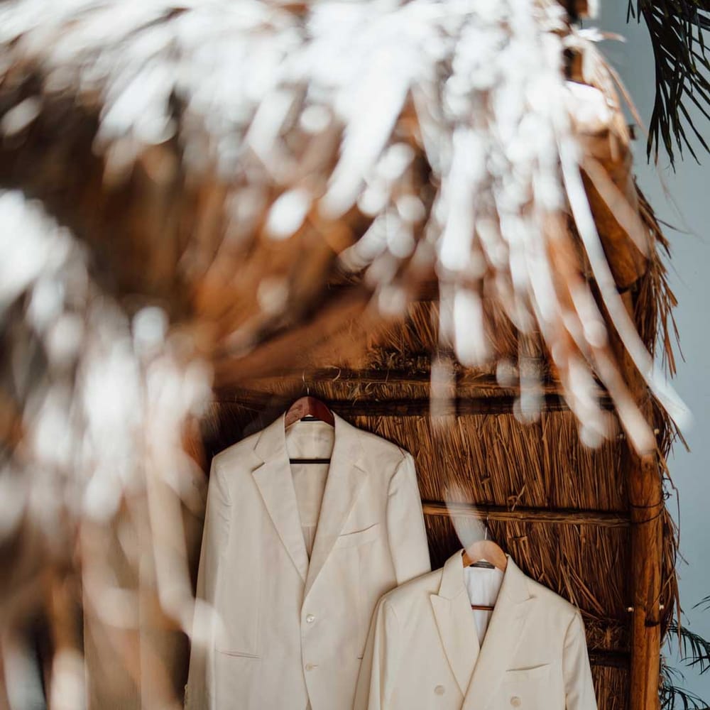 Mens white wedding suit on hangers at tropical destination beach wedding 