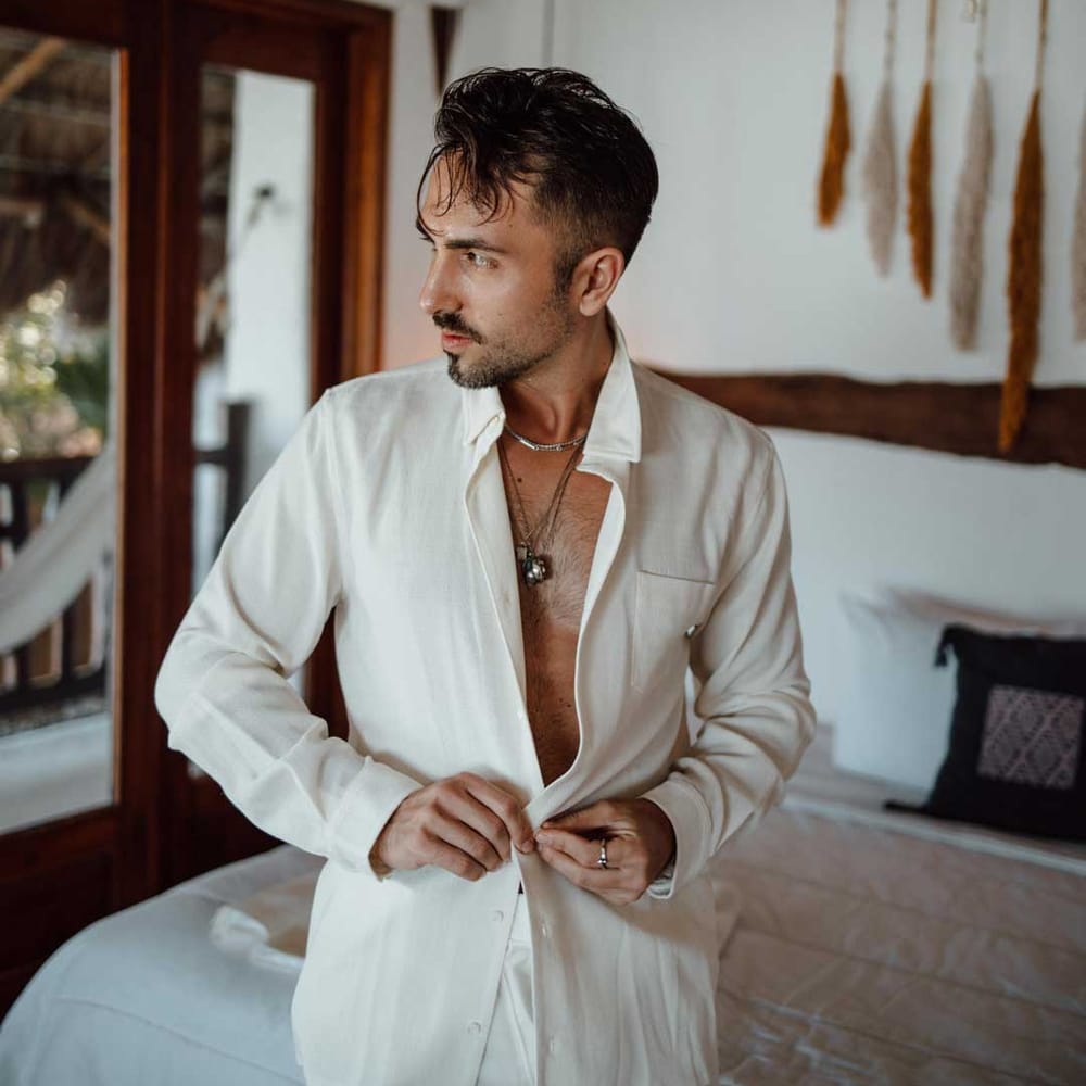 Groom putting on white linen grooms shirt at destination wedding 