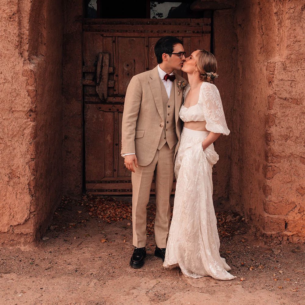 Bride with flowers in her hair wearing a crop top and maxi skirt bridal two piece with the groom leaning for a kiss 