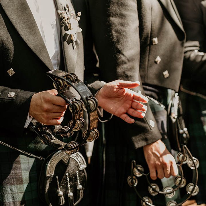 Groomsmen in green checkered kilts play tambourines at the wedding ceremony 