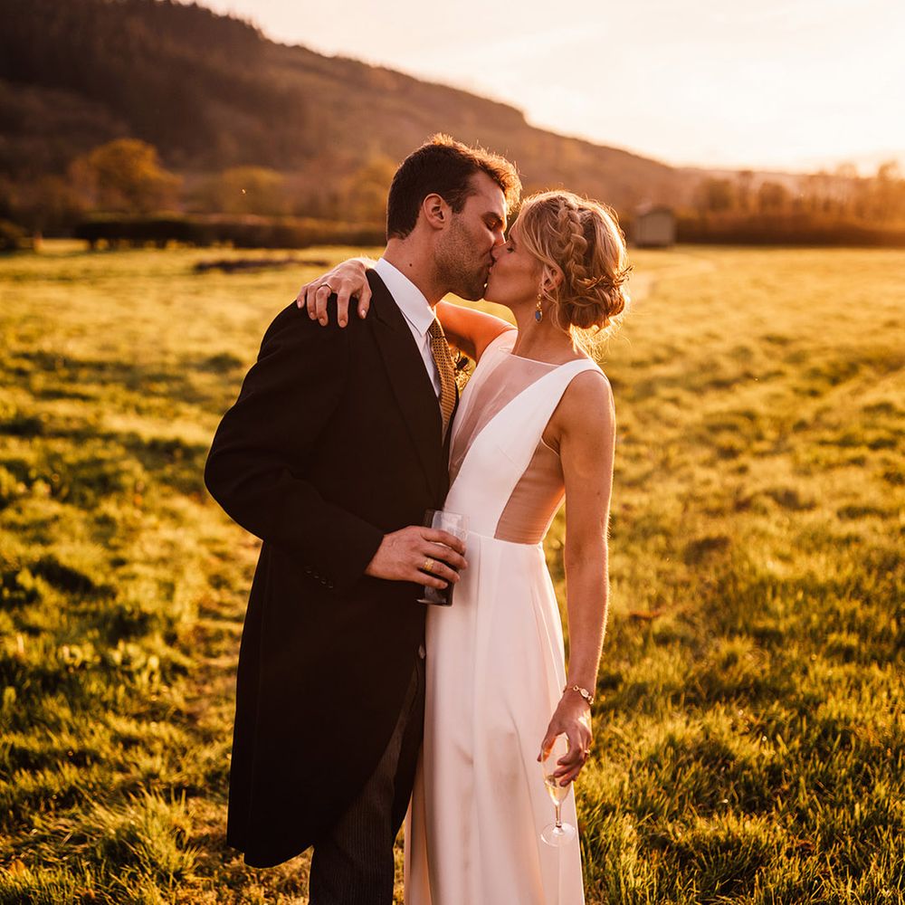 Bride with braided crown hairstyle on blonde hair kissing the groom during golden hour 