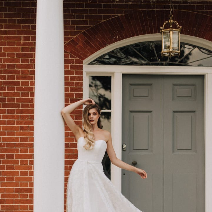 bride wears strapless feathered skirt wedding dress on the steps of Reymerston Hall
