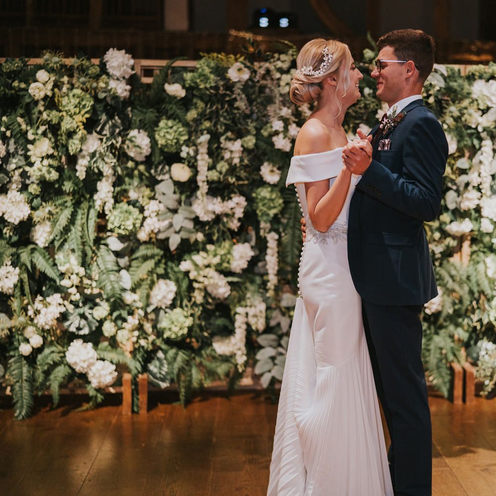 Bride & groom during their first dance with floral wall in the background