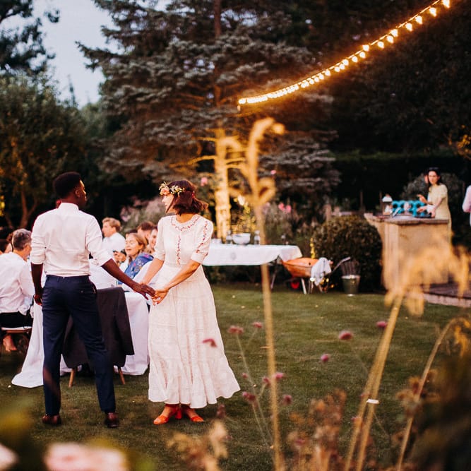 Bride and groom holding hands at their intimate garden reception with festoon light decor 