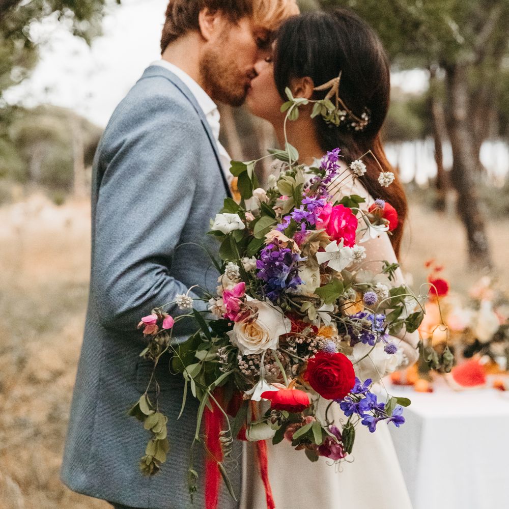 Bride & groom kiss whilst bride holds big and bold floral bouquet 