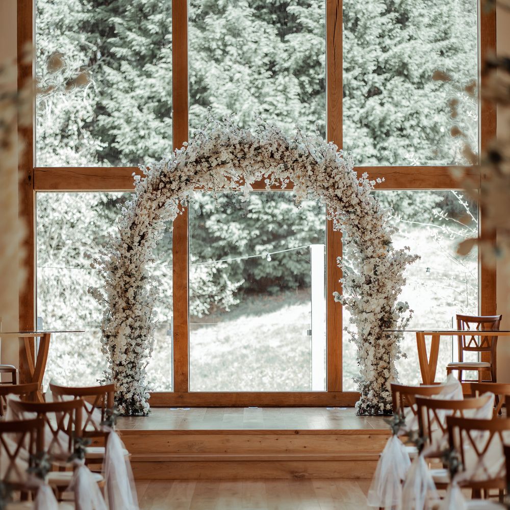 Floral archway with windows to the background and chairs lining the aisle 