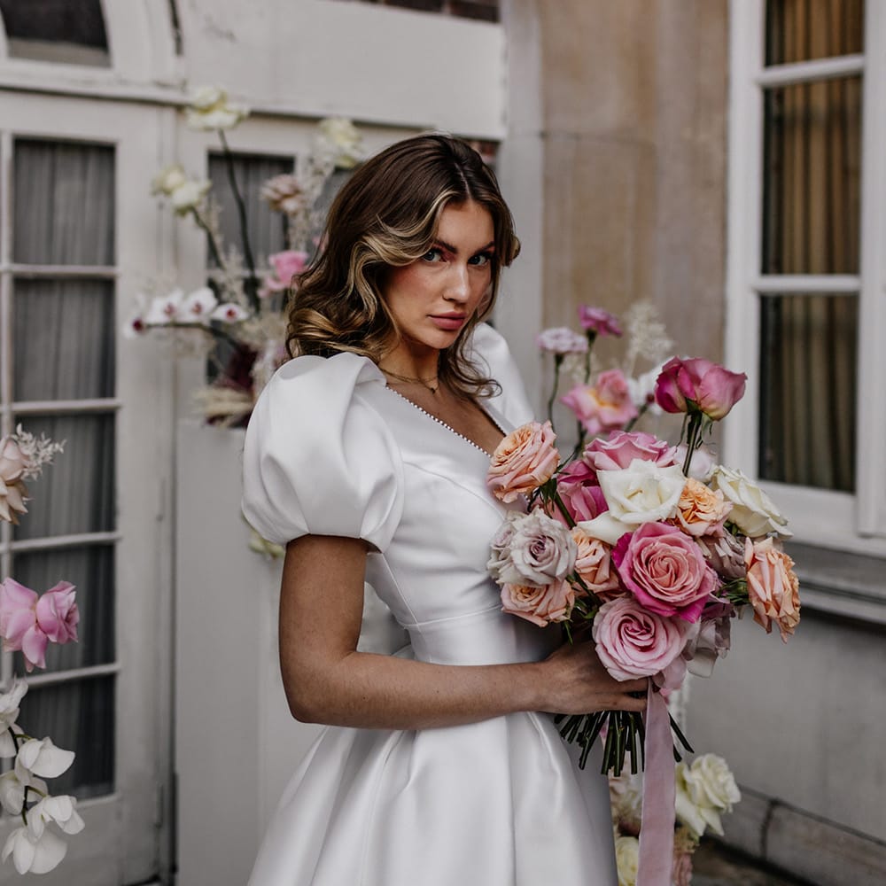 Bride holding a pink peeled rose wedding bouquet tied with ribbon 