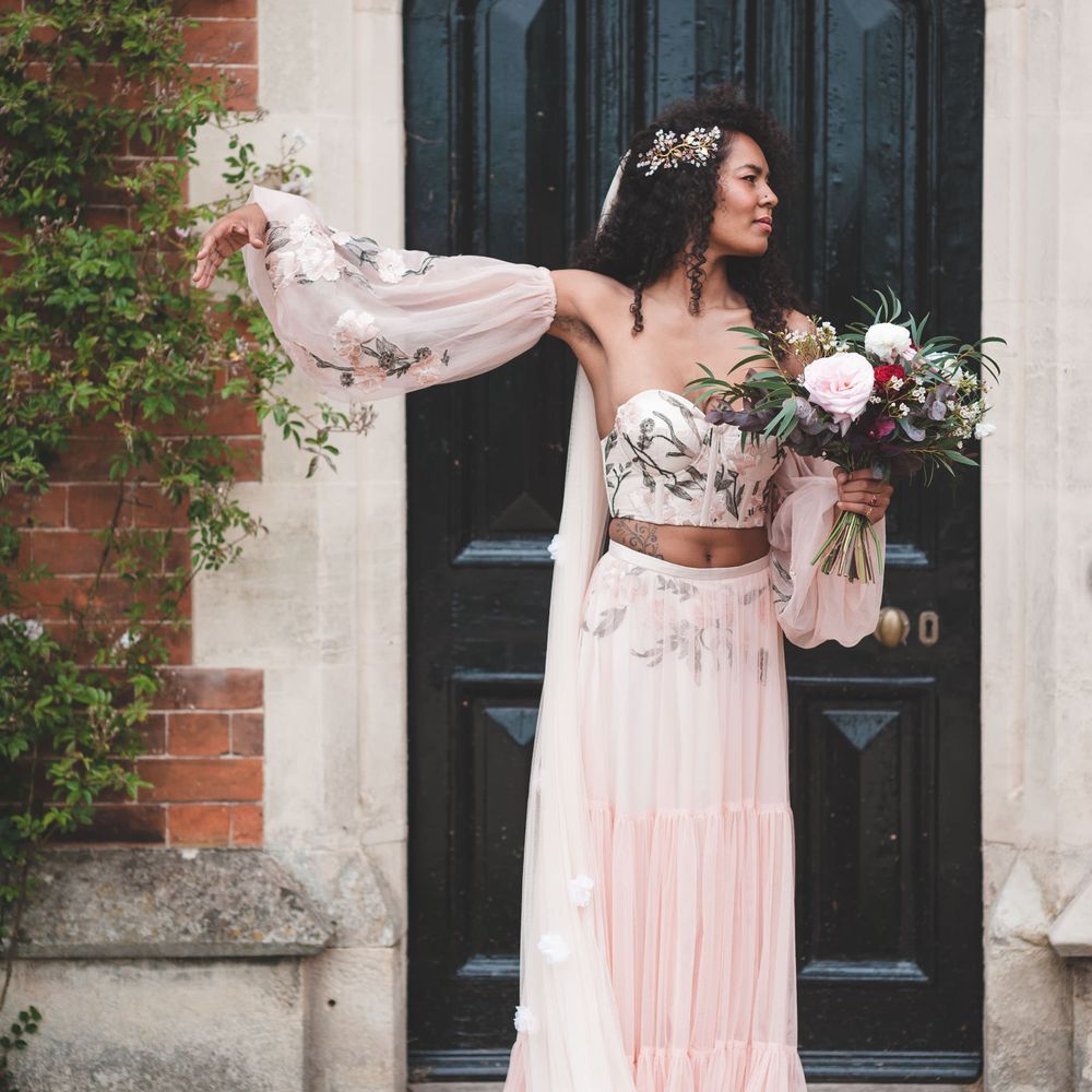 Black bride with long naturally curly hair in a blush pink with embroidery detail bridal three piece including bodice, skirt and blouson sleeves 