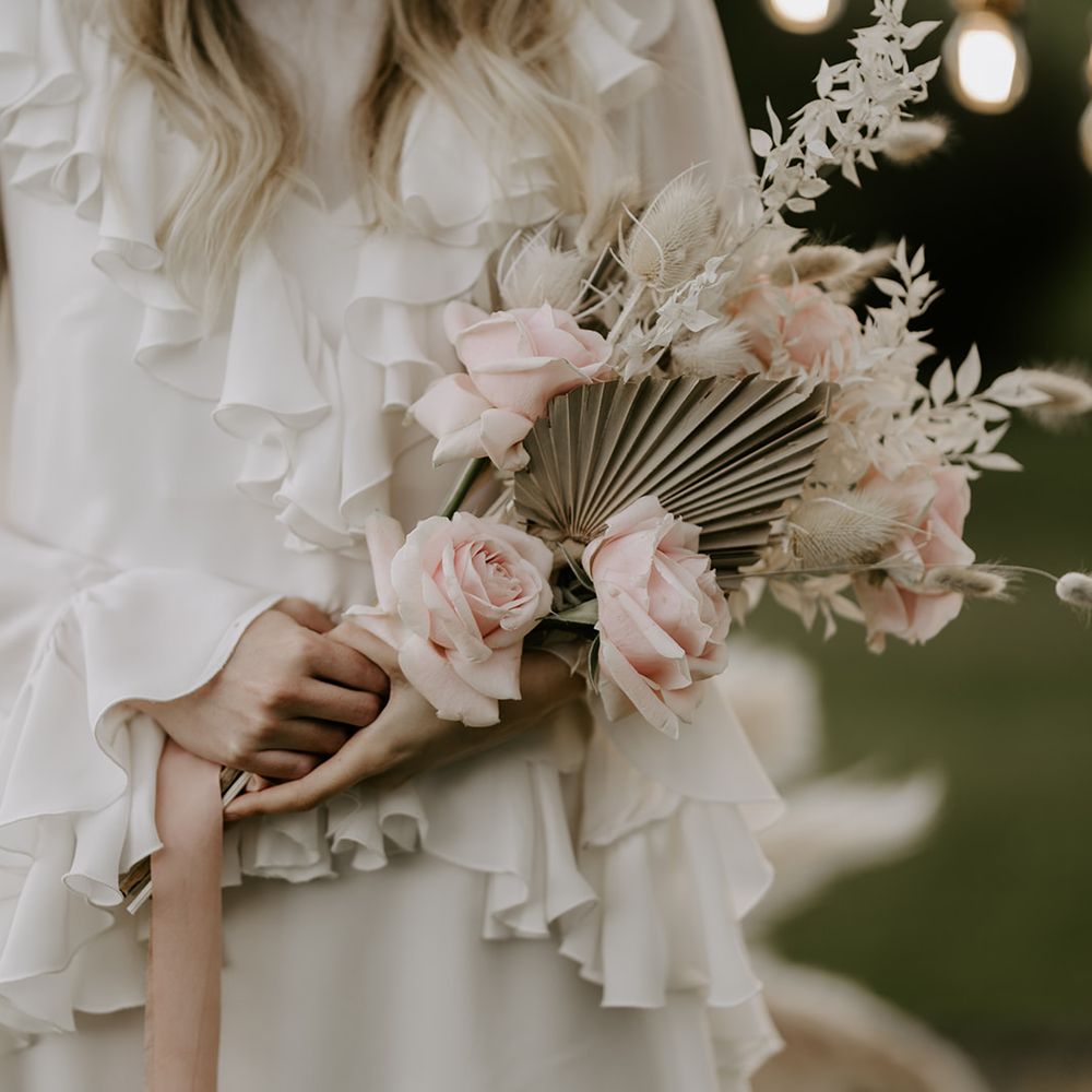 Bride in a ruffle wedding dress holding a pink rose and dried palm leave wedding bouquet 