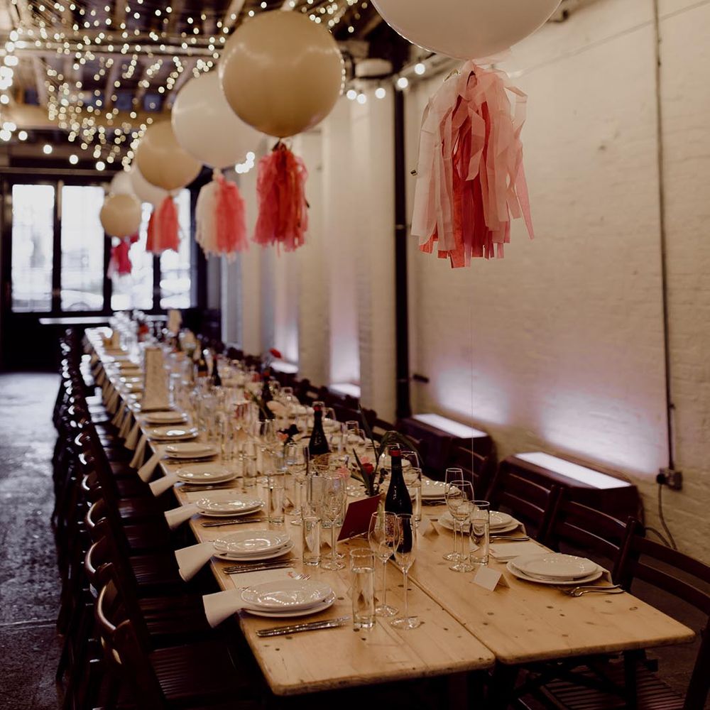 100 Barrington wedding venue decorated with white balloons and pink tissue paper tassels, fairy lights and long banquet tables with simple table settings