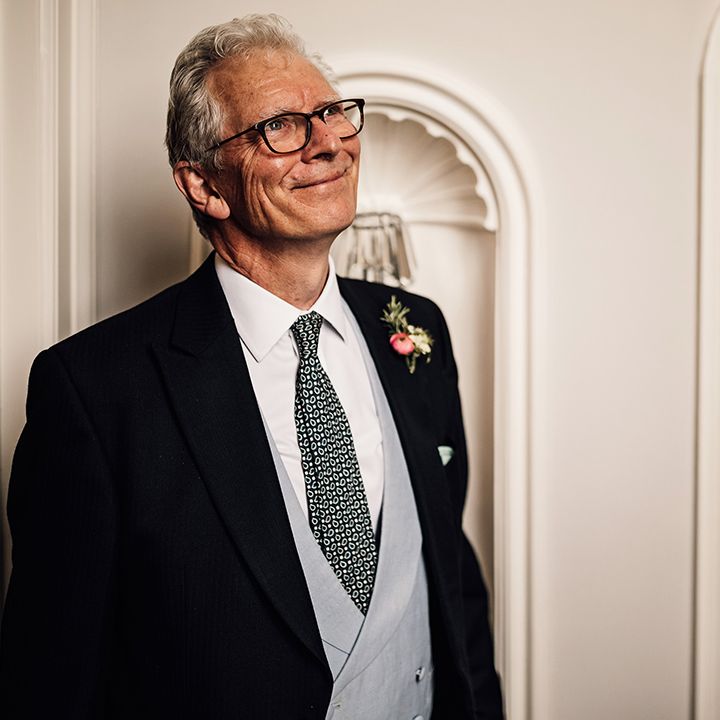 Father of the bride in black suit jacket, grey waistcoat and black and white patterned tie smiles as he gets the first look at the bride 