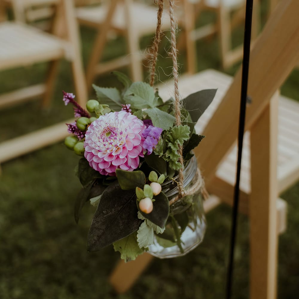 Small glass mason jars full of pink and purple flowers hanging on string for aisle wedding decoration 