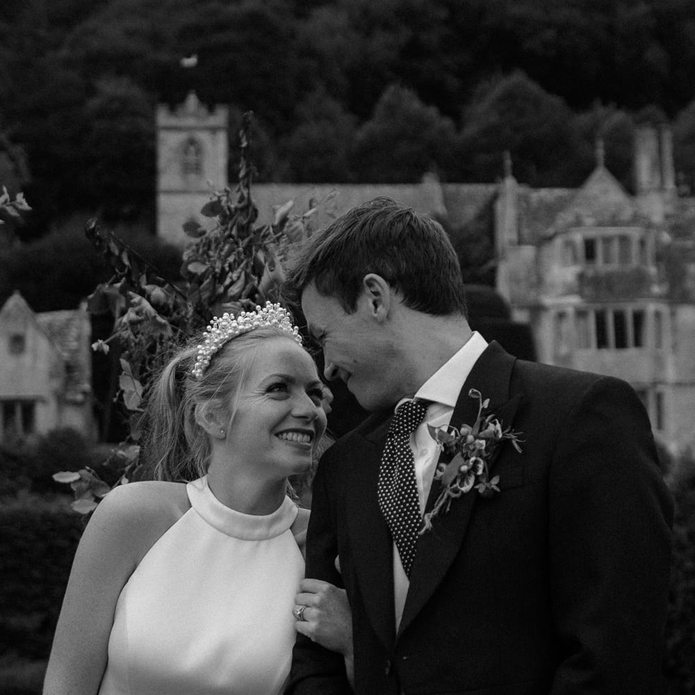 Bride and groom link arms and smile at each other with groom in morning suit and bride in halter neck wedding dress 