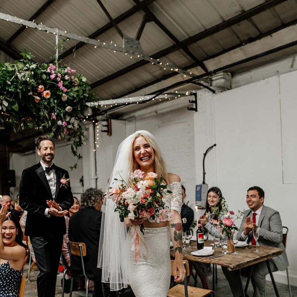 Bride in boho two piece lace bridal outfit with large colourful mixed bouquet laughing and smiling during wedding reception