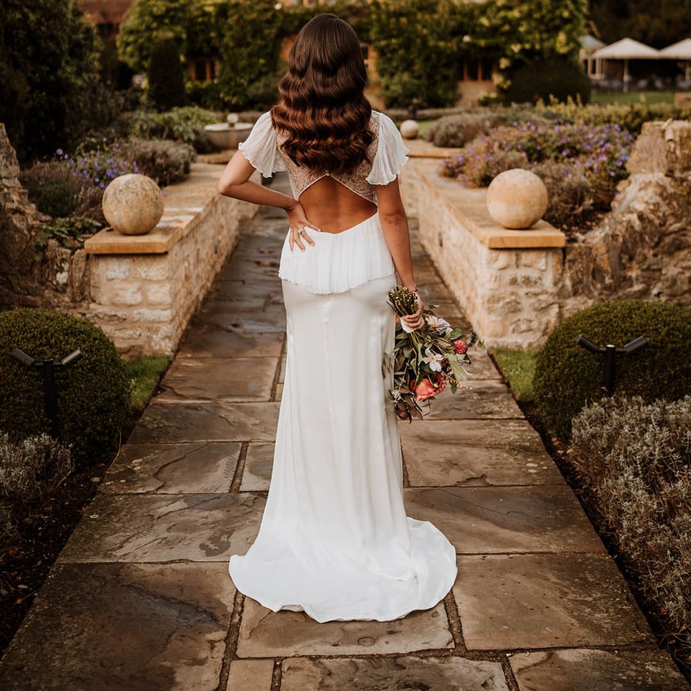 Bride in open back wedding dress with button details and butterfly sleeves posing at Oxfordshire wedding venue