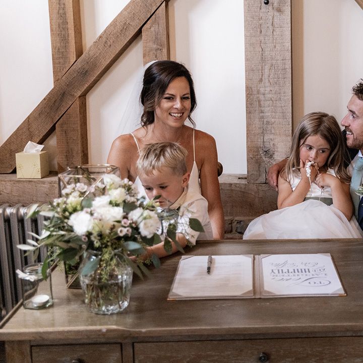 Chloe Bruce & her husband sit with their children as they sign marriage certificate after barn wedding ceremony