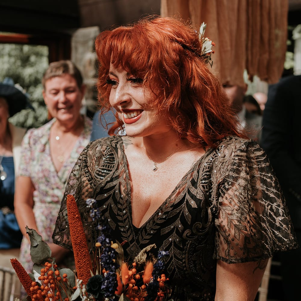 Bride in embellished v neck black dress for wedding in Devon with orange and yellow dried flower wedding bouquet 