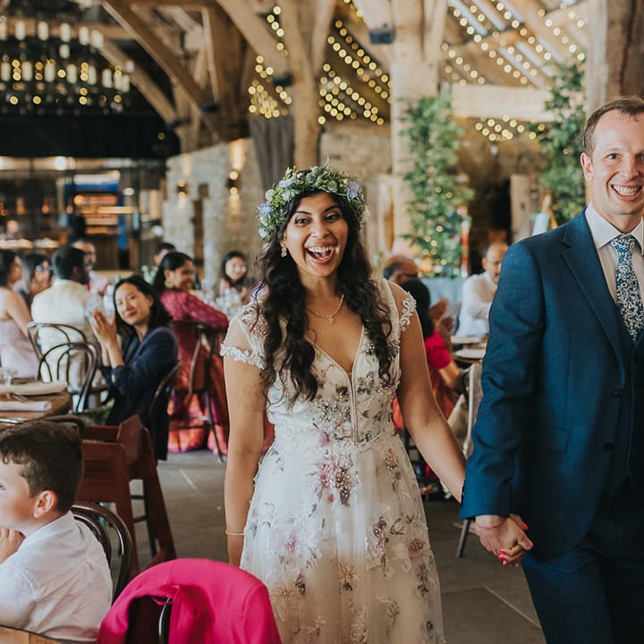 British Indian bride in a Savin London Amelia Dress entering the wedding reception with her groom in a light blue suit 