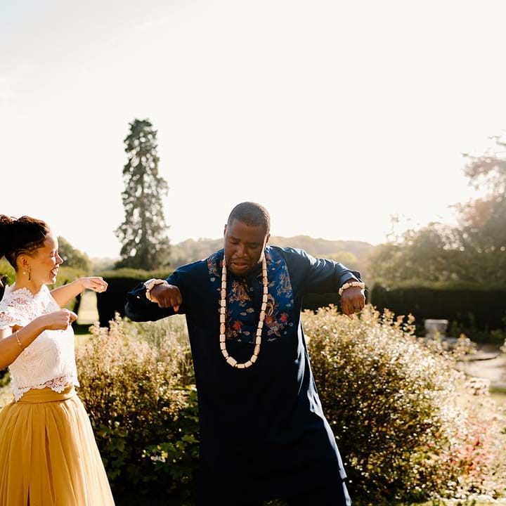 Groom in traditional Nigerian wedding outfit with off white wedding beads necklace dancing with bride in white mesh lace bridal crop top and yellow wedding skirt at Broadfield Court