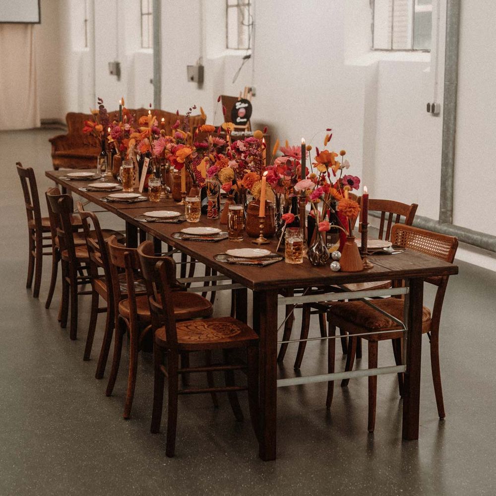 German auction house wedding venue with rustic wedding tablescape with vinyl record place mats, gold rimmed plates, gold cutlery, colourful pink, red and orange floral centrepieces in bottles and tapered candles 