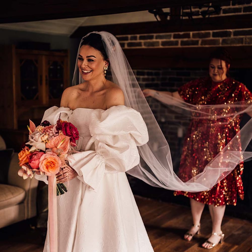 Bride in a puff sleeve Jesus Peiro wedding dress holding colourful wedding bouquet with veil 