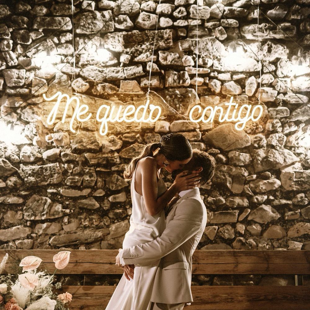 Groom in a beige suit picking up his bride in a slip dress in front of a neon sign 