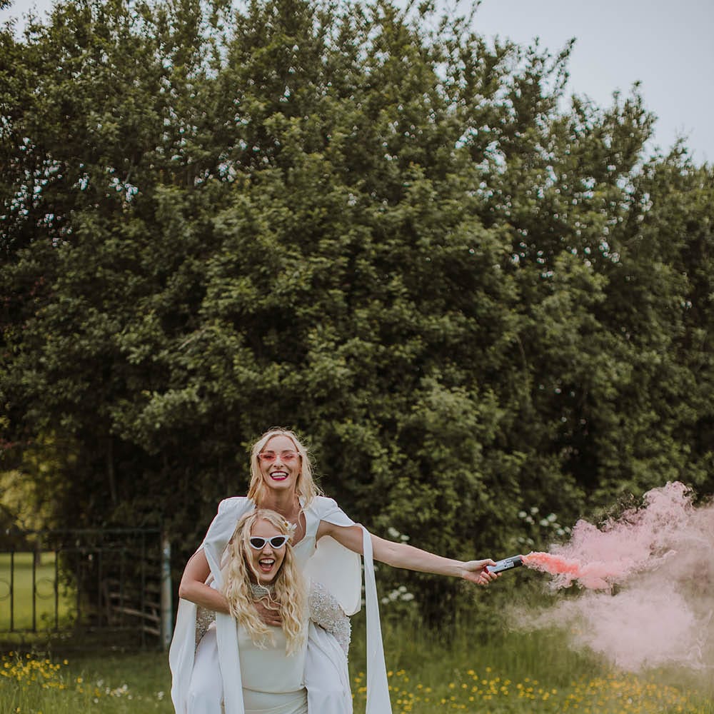 LGBTQI+ couple portrait in a field with a pink smoke bomb 
