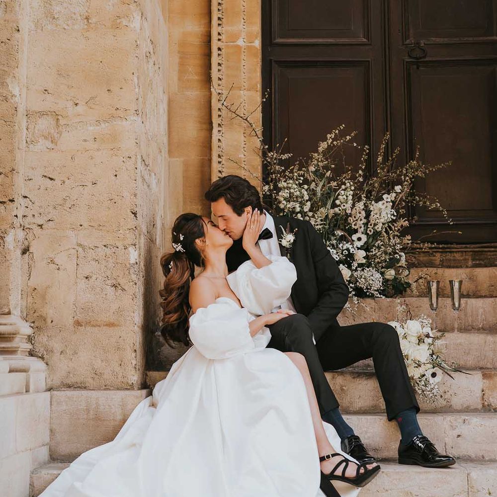 Bride in a stylish wedding dress with front split and detachable puff sleeves kissing her groom on the steps at Bodleian wedding venue in Oxford