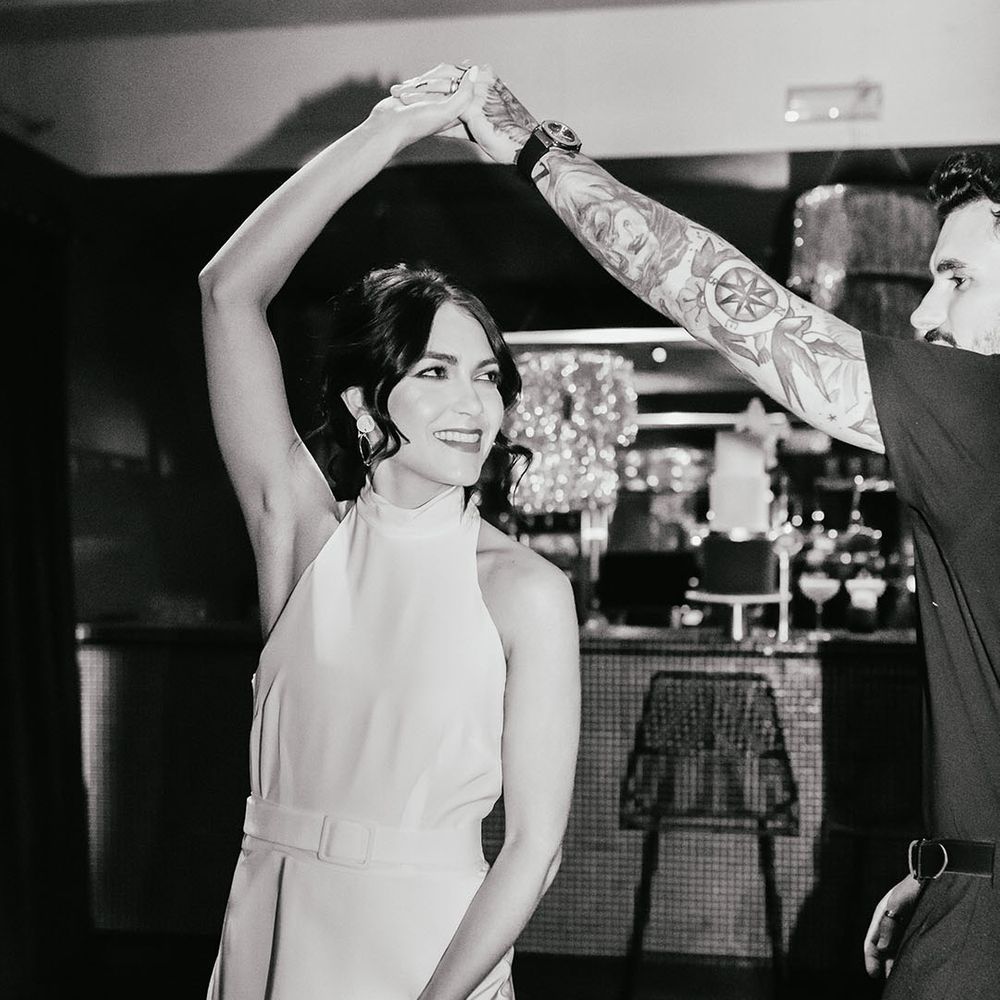 Black and white portrait of the groom in a black short sleeve shirt twirling his bride in a halterneck wedding dress 