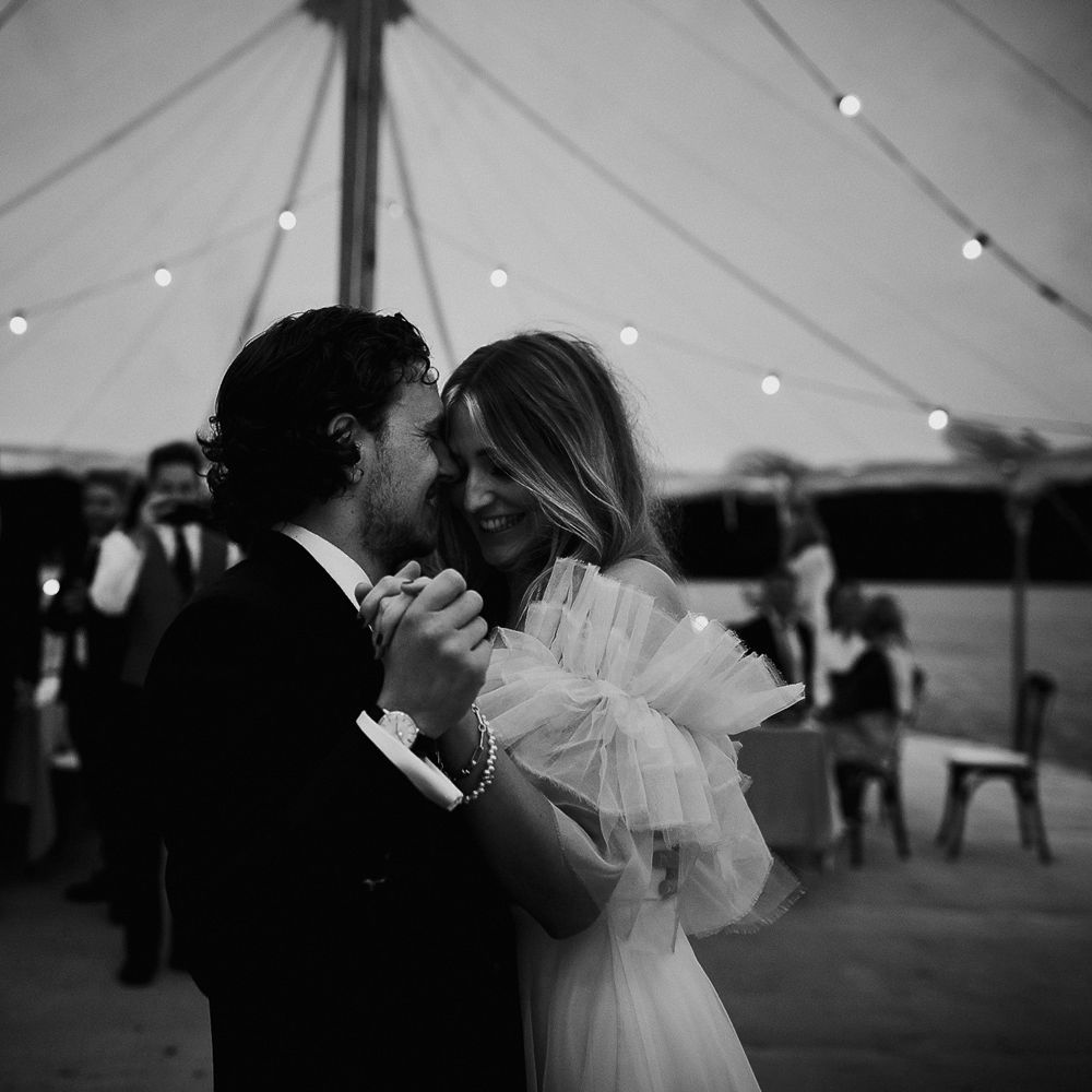 Bride in white Halfpenny London Mayfair dress with ruffle sleeves dances with groom in suit during marquee garden wedding reception in Cornwall
