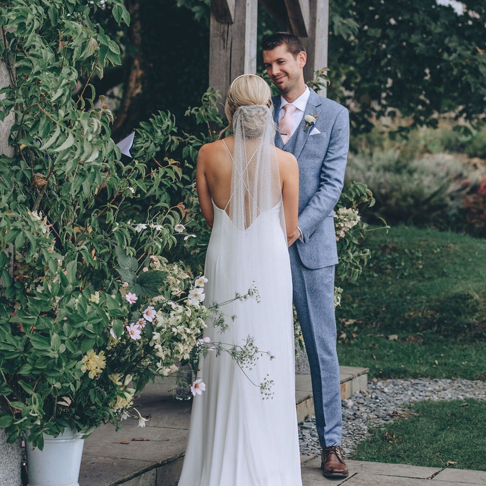 Cross back Rime Arodaky wedding dress with pinned updo and pale suit for groom