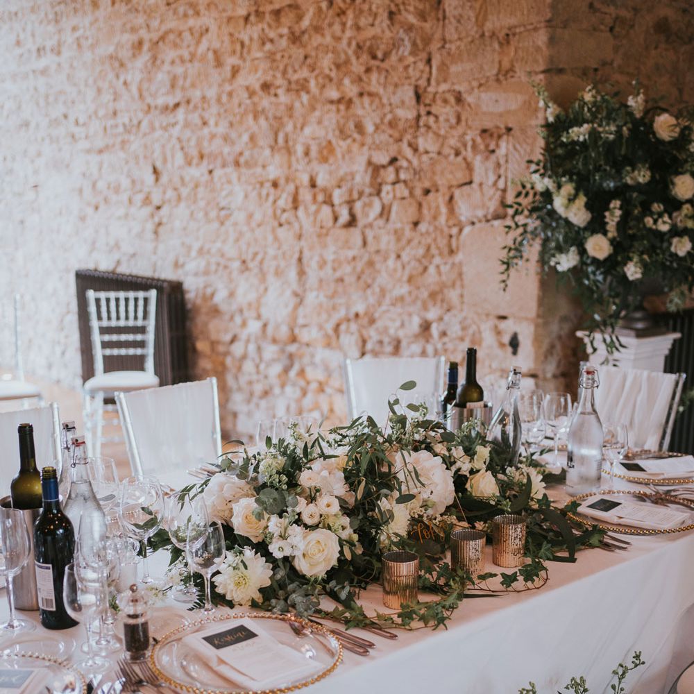 White and green floral centrepiece on white tables with gold tableware for Notley Abbey wedding reception