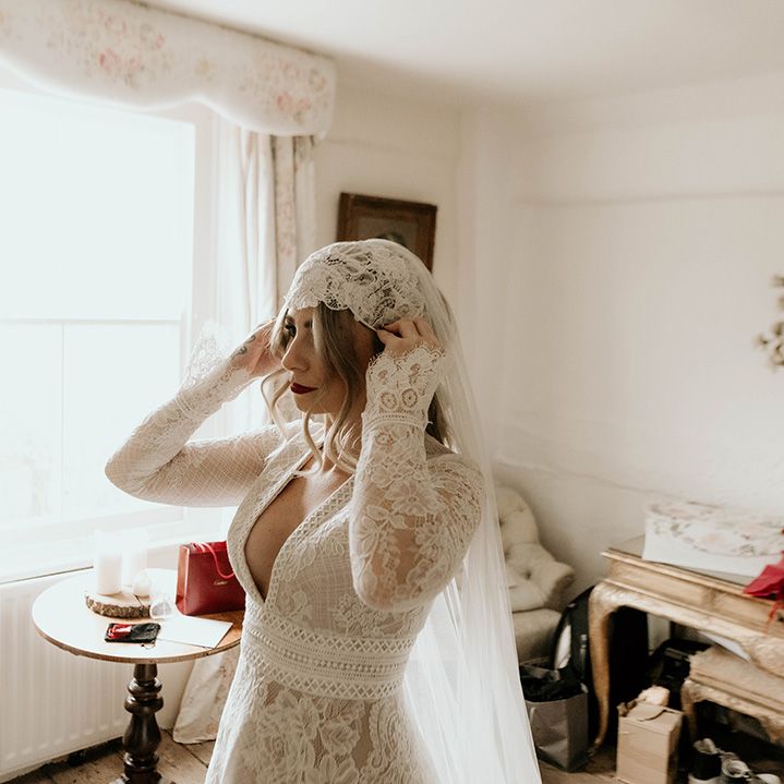 Bride in a long sleeve wedding dress with bell sleeves putting on her Juliet cap veil 