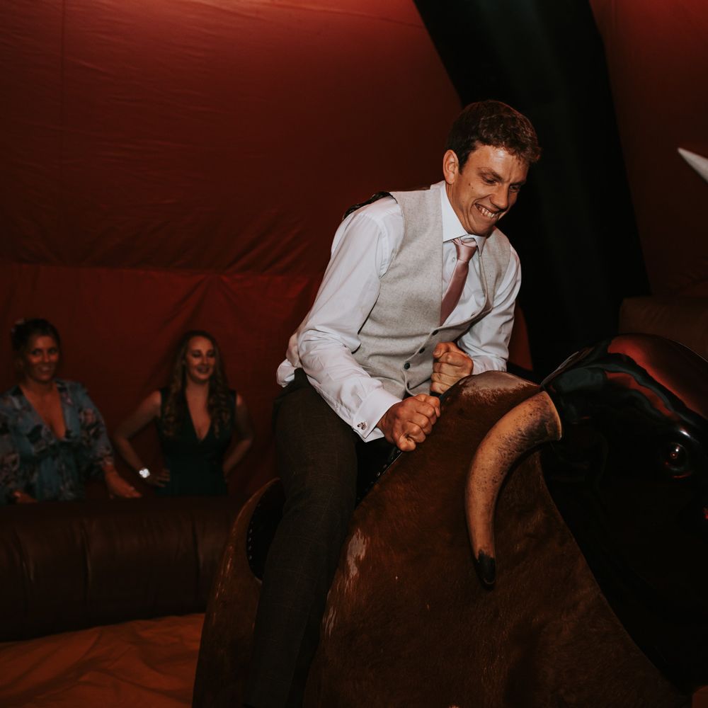 Wedding guest in waistcoat and white shirt on bucking bronco at barn wedding in the Lake District